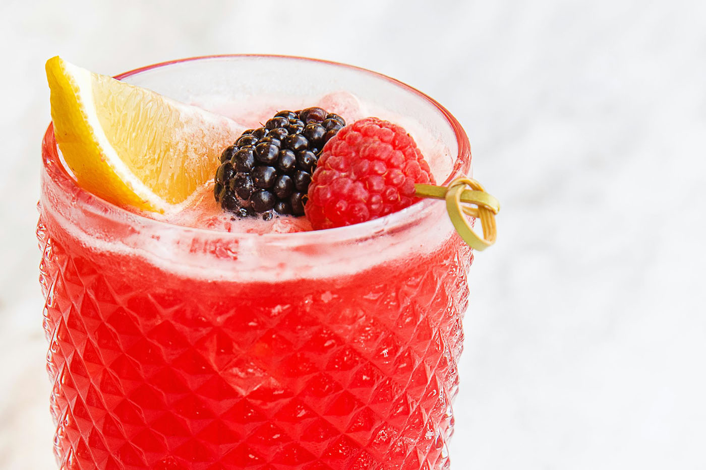 Red berry-flavoured beverage with lemon, blackberry and raspberry garnish, highlighting natural colours in drinks.