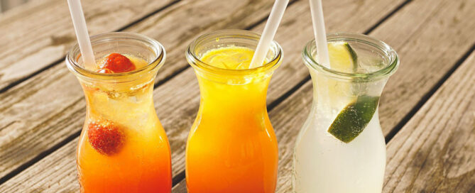 Three colourful fruit juice drinks in glass bottles with fresh fruit and citrus, symbolising natural beverage formulations.